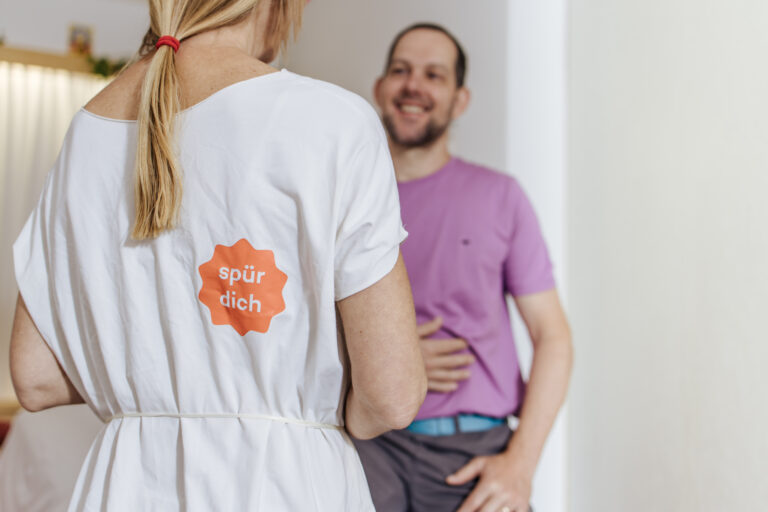 Person mit „spür dich“-Aufdruck im Gespräch mit einem sitzenden Mann