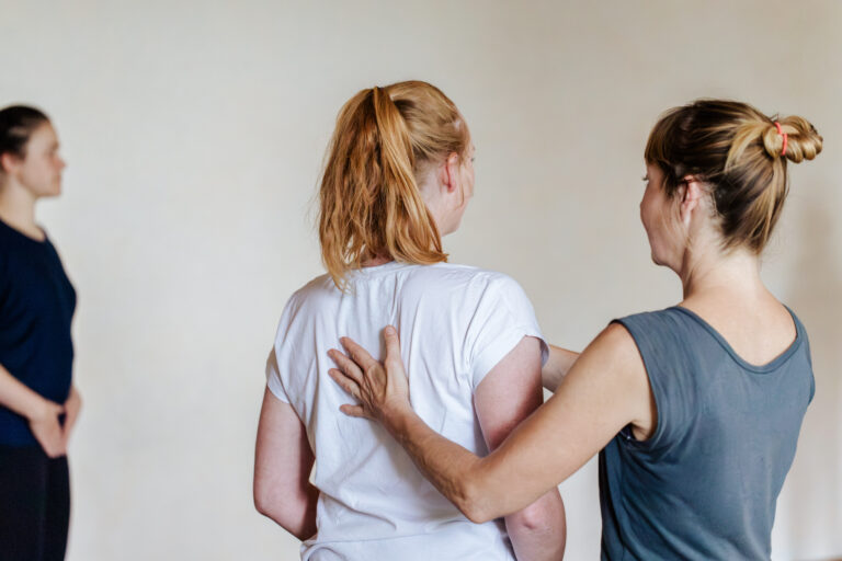 Pilates-Trainerin gibt einer Teilnehmerin in einer Gruppe eine Haltungsanleitung