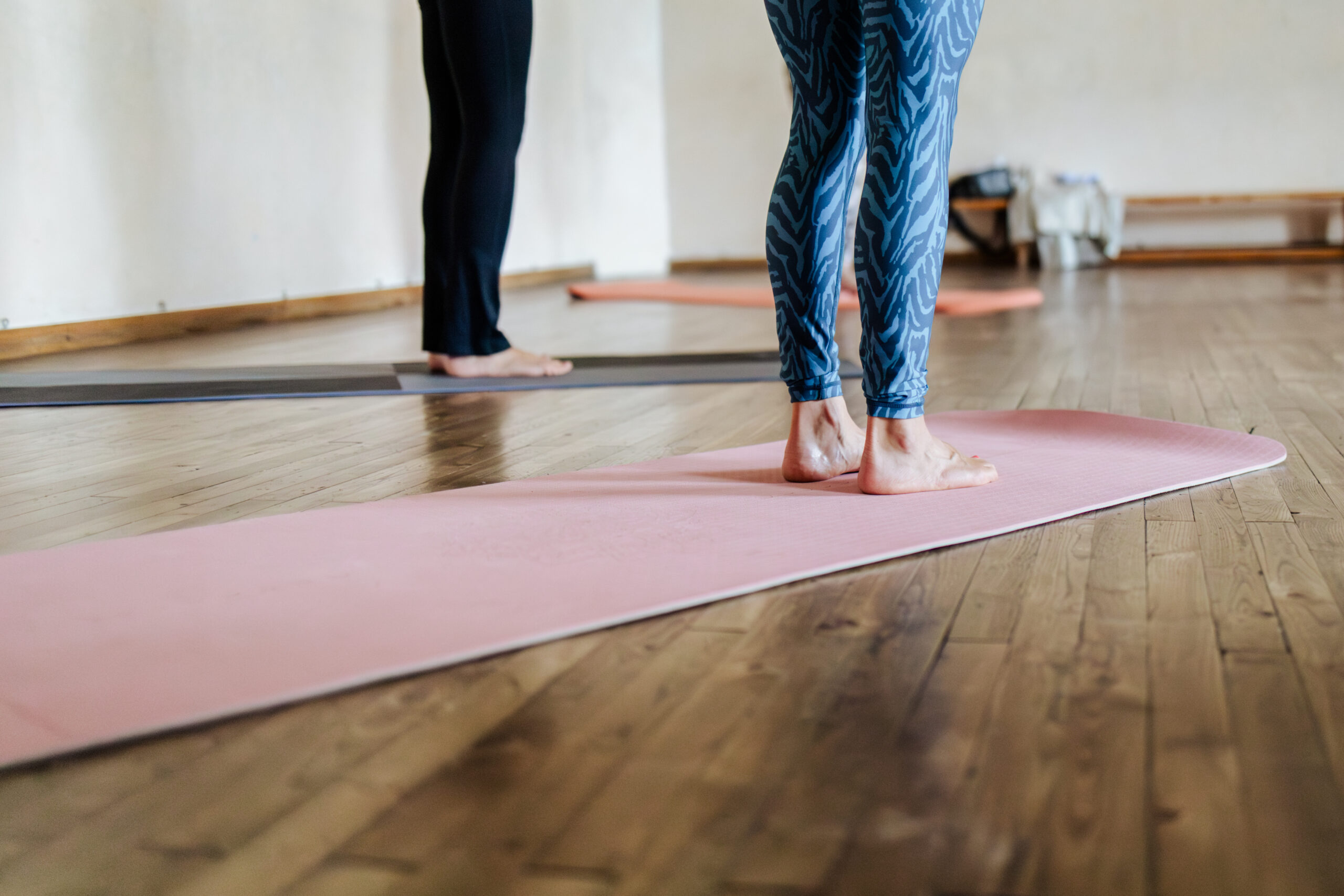 Doris leitet eine Pilatesübung mit über dem Kopf zusammengeführten Händen an; im Vordergrund folgt eine Teilnehmerin der Bewegung.